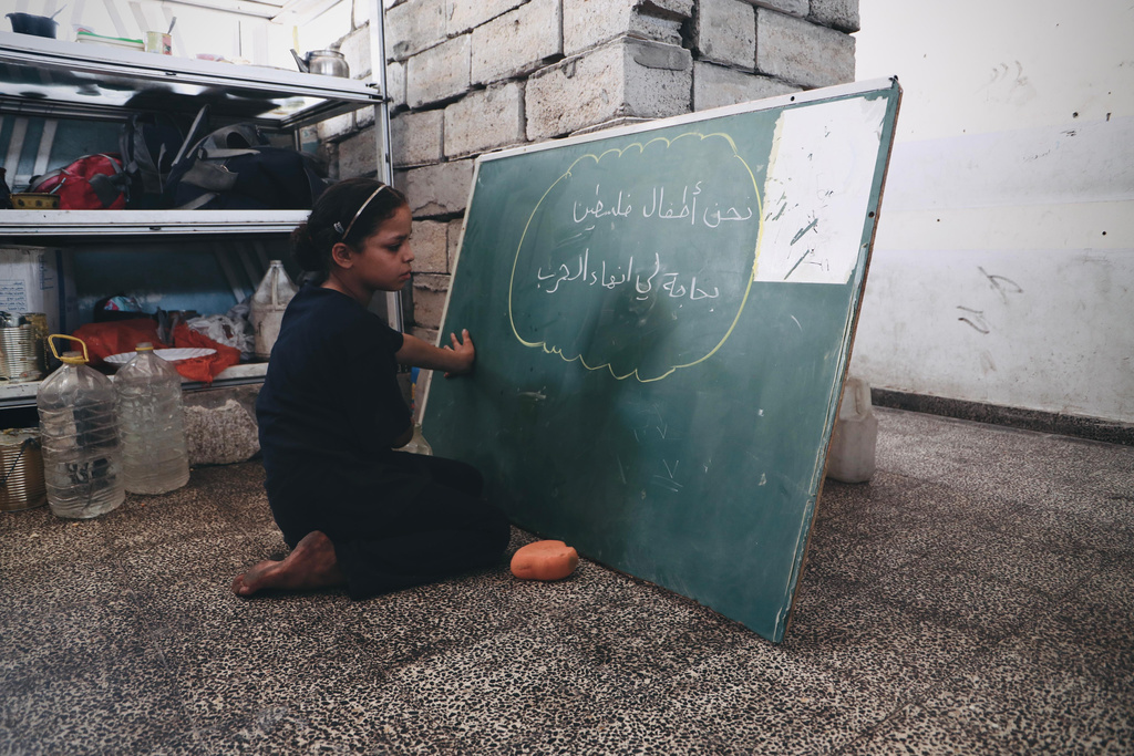 طالبة تكتب على لوح في مدرسة بمدينة خان يونس "نحن أطفال فلسطين بحاجة إلى إنهاء الحرب" (تصوير: الأونروا)